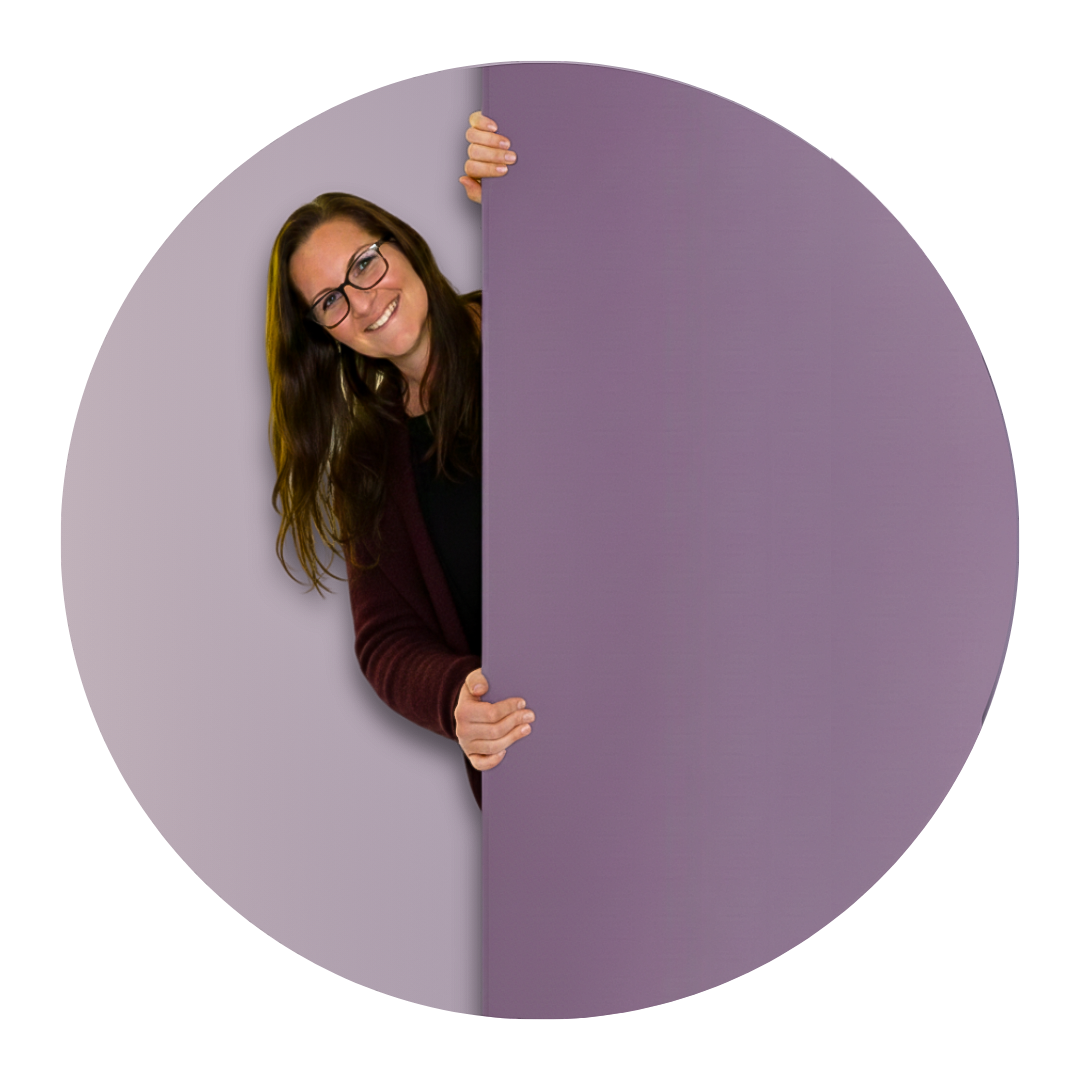 Kvinna som tittar fram bakom en vägg. Kvinnan är glad och har glasögon 