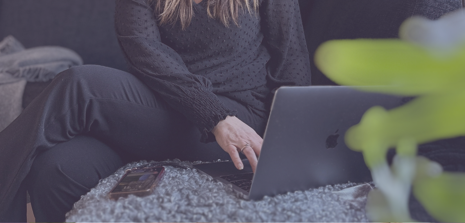 Kvinna som sitter i en soffa och skriver på en laptopp, man ser bara kvinnans överkropp och ben samt armar. 