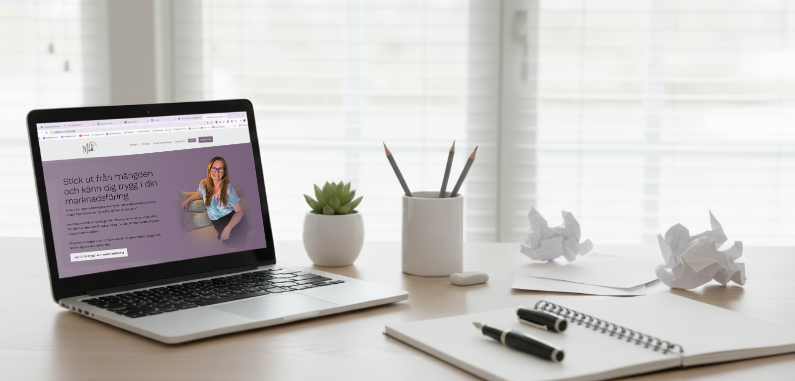 En dator med bild på startsidan för Mwh Kommunikation samt ett block med en penna